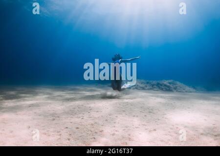 Lady freediver with fins posing and glides underwater in blue ocean with sunlight. Stock Photo