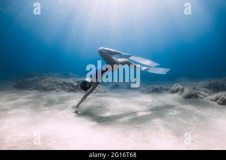 Lady freediver with fins posing and glides underwater in blue ocean with sunlight. Stock Photo