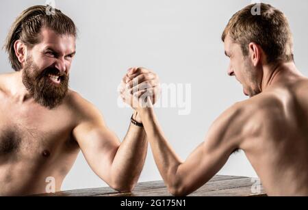 Heavily muscled bearded man arm wrestling a puny weak man. Arms wrestling thin hand, big strong arm in studio. Two man's hands clasped arm wrestling