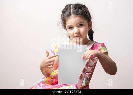 Little girl pointing a story book with blank cover sit on chair, editable mock-up series template ready for your design, cover selection path included Stock Photo