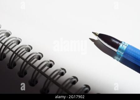 Blue ball pen on a bright sunny white notebook paper. Stock Photo