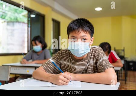 Asian boy in classroom with face mask back at school after covid-19 quarantine and lockdown. Stock Photo
