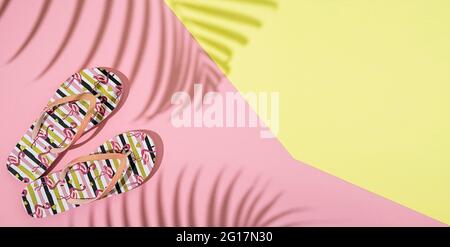 Flip flops and palm leaf shadows on pink and yellow background, flatly with copy space Stock Photo