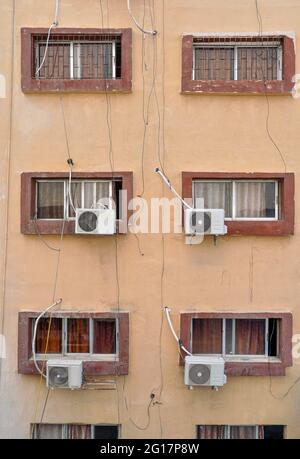 Air conditioning external units with large fans on old building facade wall near windows, many untidy cables near Stock Photo