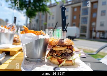 eating street food burger on the street with sweet potato fries . Stock Photo