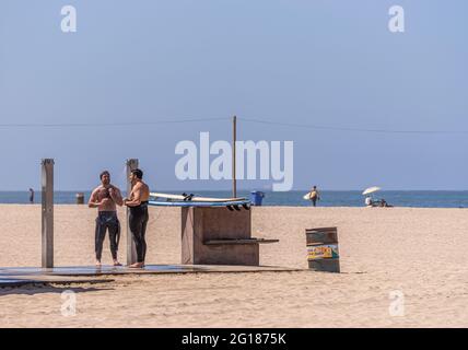 Santa Monica, CA, USA - June 20, 2013: Closeup of couple of male surfers take shower on sandy beach under blue sky. Stock Photo