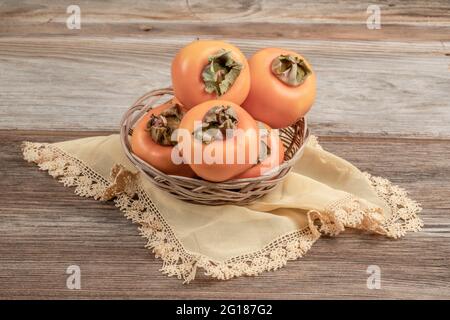 ripe persimmon fruits in a basket on wooden table with copy space Stock Photo