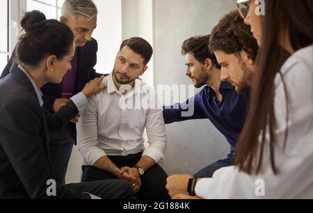 Group of people sitting in a circle supporting and comforting a sad upset young man Stock Photo