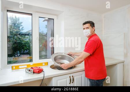 white man installs round single stainless steel sink into a cut-out hole  Stock Photo