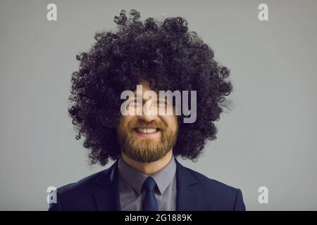 Studio portrait of happy businessman in suit and crazy curly wig smiling at camera Stock Photo