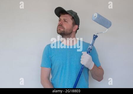 Young painter in blue t-shirt, cap and gloves painting a wall with paint roller. Stock Photo