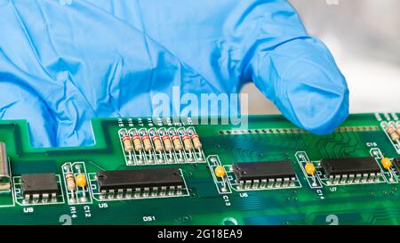Electronic components on green printed circuit board on human hand. Close-up of black IC chips, capacitors or resistors on PCB of computer keyboard. Stock Photo