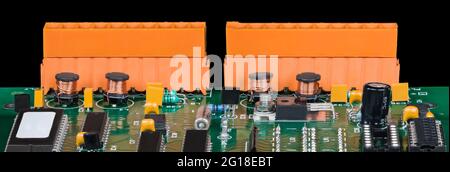 Panoramic detail of electronic components on a green circuit board. Chips, cylindrical coils, transistors, capacitors and two orange terminal blocks. Stock Photo