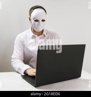A man in a mask works behind a laptop, the concept of anonymity on the Internet. Stock Photo