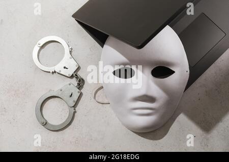 White mask on a laptop and handcuffs on the table, the concept on the topic of crimes and anonymity in the field of information technology. Stock Photo