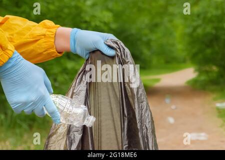 Volunteer hands picks up plastic garbage from grass in park. Volunteer cleaning up trash a forest. Plastic waste. Male collects garbage people Stock Photo