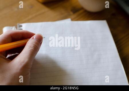 Female hand writing with yellow pencil on a blank sheet of lined paper in notebook on wood desk Stock Photo