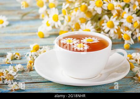 Daisy flowers in a white cup of tea, chamomile herbs on wooden background. Herbal medicine. Healthy lifestyle concept. Stock Photo
