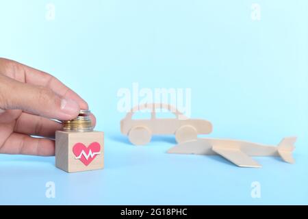 Invest on health over travel, car and material things concept. Human hand putting coins on a healthcare icon. Stock Photo