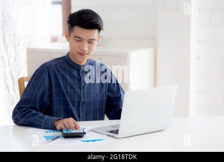 Young asian business man working using calculator for planning accountant, graph for finance and report statistics, investment and profit of income, b Stock Photo