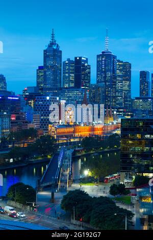 A night view of Melbourne, Australia, including CBD highrise buildings and Flinders Street Station, seen with the Yarra River and Sandridge Bridge.