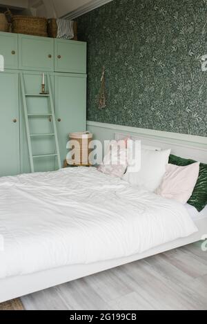 The interior of the bedroom is in a modern style. Mint wardrobe and white bed with colorful pillows Stock Photo