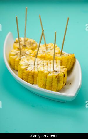 Corn, a snack made using ripe corn and garnished with chilli flakes and honey arranged in a white beautiful tableware  which is placed on a solid ice Stock Photo