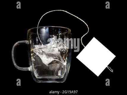 A tea bag with empty label fall into a glass mug with hot water,  on a black background Stock Photo