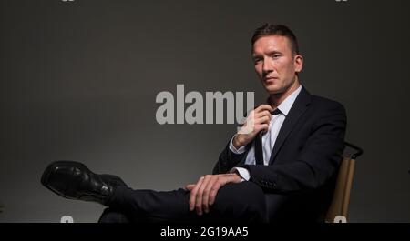 Portrait of a pensive confident man, in a business suit, sitting cross-legged against a dark background. Stock Photo