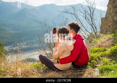 Young traveler couple resting and taking selfie in the mountains. Man and woman hiking with backpacks on a beautiful rocky trail. Family local travel Stock Photo