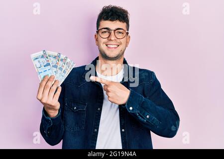 Young hispanic man holding peruvian sol banknotes smiling happy pointing with hand and finger Stock Photo