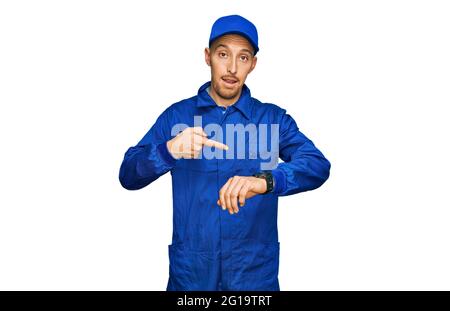 Bald man with beard wearing builder jumpsuit uniform in hurry pointing to watch time, impatience, upset and angry for deadline delay Stock Photo