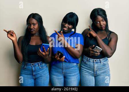 Three young african american friends using smartphone pointing aside worried and nervous with forefinger, concerned and surprised expression Stock Photo