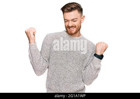Young redhead man wearing casual winter sweater very happy and excited doing winner gesture with arms raised, smiling and screaming for success. celeb Stock Photo