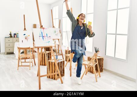 Middle age artist woman smiling happy and dancing painting at art studio. Stock Photo