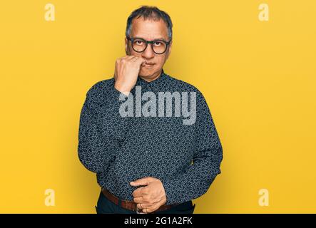 Middle age indian man wearing casual clothes and glasses looking stressed and nervous with hands on mouth biting nails. anxiety problem. Stock Photo