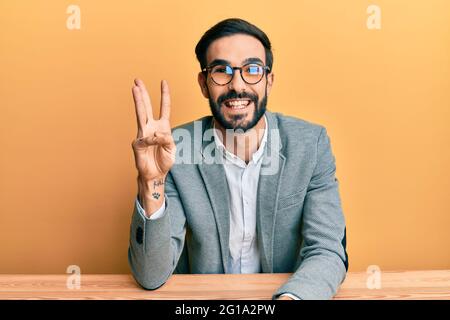 Young hispanic man working at the office showing and pointing up with fingers number three while smiling confident and happy. Stock Photo