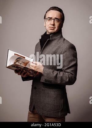 Portrait of snobby intellectual man literary critic in checkered jacket and black scarf looking through new book Stock Photo