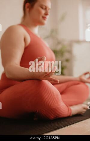Woman sitting cross-legged on mat meditating in yoga posture. Woman practicing yoga with focus on hand. Stock Photo