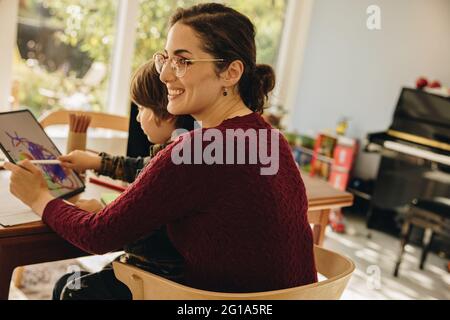 Woman sitting with son drawing on her digital tablet. Mother with kid sitting at tablet using tablet computer. Stock Photo