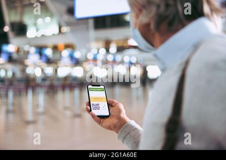 Over the shoulder view of a man holding his mobile phone with vaccine passport on display. Businessman at airport holding a smart phone with a digital Stock Photo