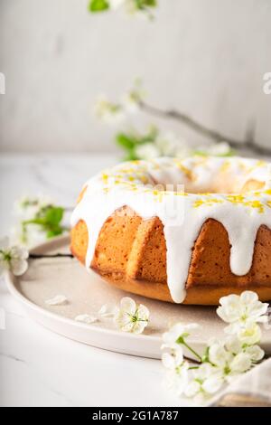 Fresh homemade lemon bundt cake decorated with white glaze and zest on white marble background with branches of blossoming plum. Stock Photo