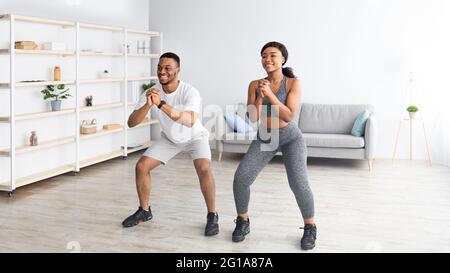 Fit black couple in sportswear doing squat exercises at home gym during covid, panorama Stock Photo