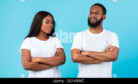 Offended black couple standing with crossed arms, blue studio wall Stock Photo