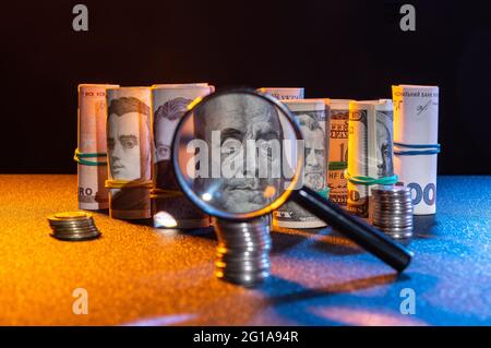 Money through a magnifying glass. Banknotes and coins on the table. Low key. Front view. Stock Photo
