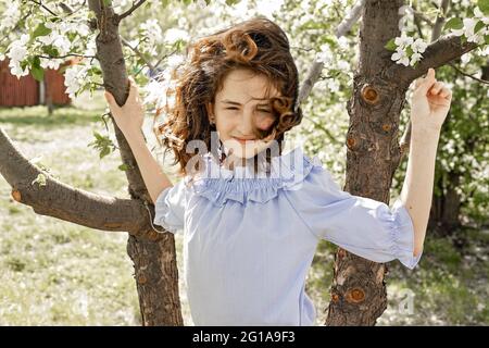 Lifestyle photo. Cute pretty smiling young brunette girl in a blooming garden. Spring photo shot against the background of blooming apple trees. Happy Stock Photo