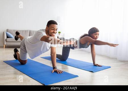Fit black couple stretching their arms and legs, doing yoga or pilates on mat indoors. Stay home hobbies Stock Photo