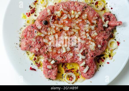 Minced meat with fresh spring onions and spices in the shape of a pig on the white plate, a creatively prepared burger in an interesting shape, funny Stock Photo
