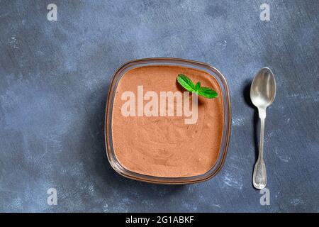 A bowl with traditional French chocolate mousse with a mint leaf and a silver spoon on blue background, top view Stock Photo