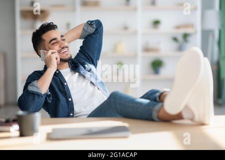 Relaxed arab guy talking on phone while having break Stock Photo